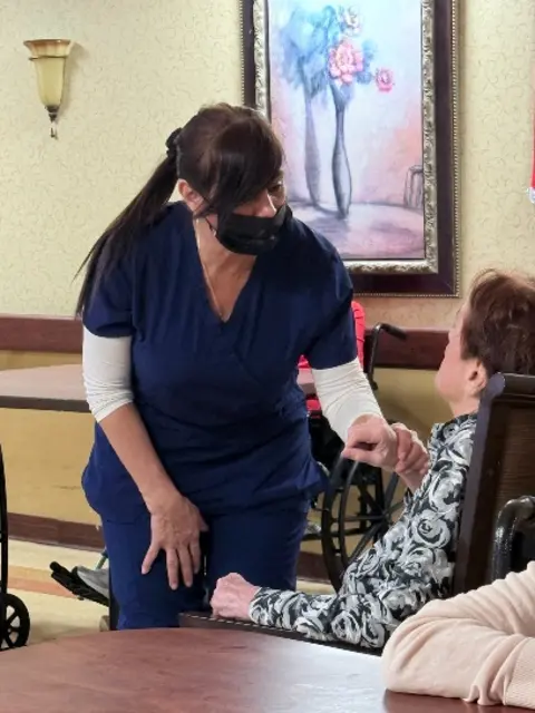 Geraldine Arcia in nursing scrubs assisting an older adult